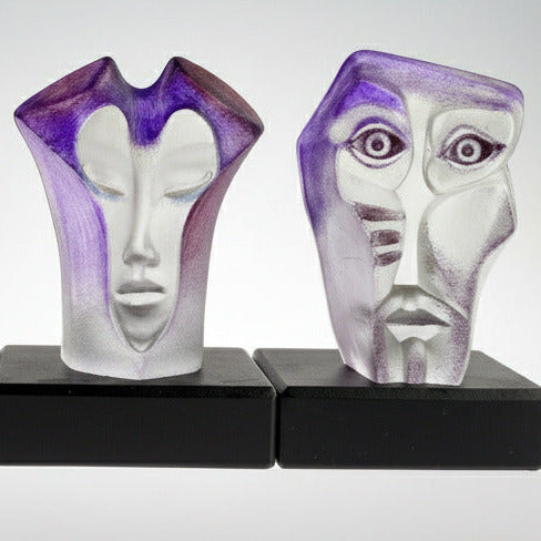 two abstract glass face sculptures on a black base against a light gray background