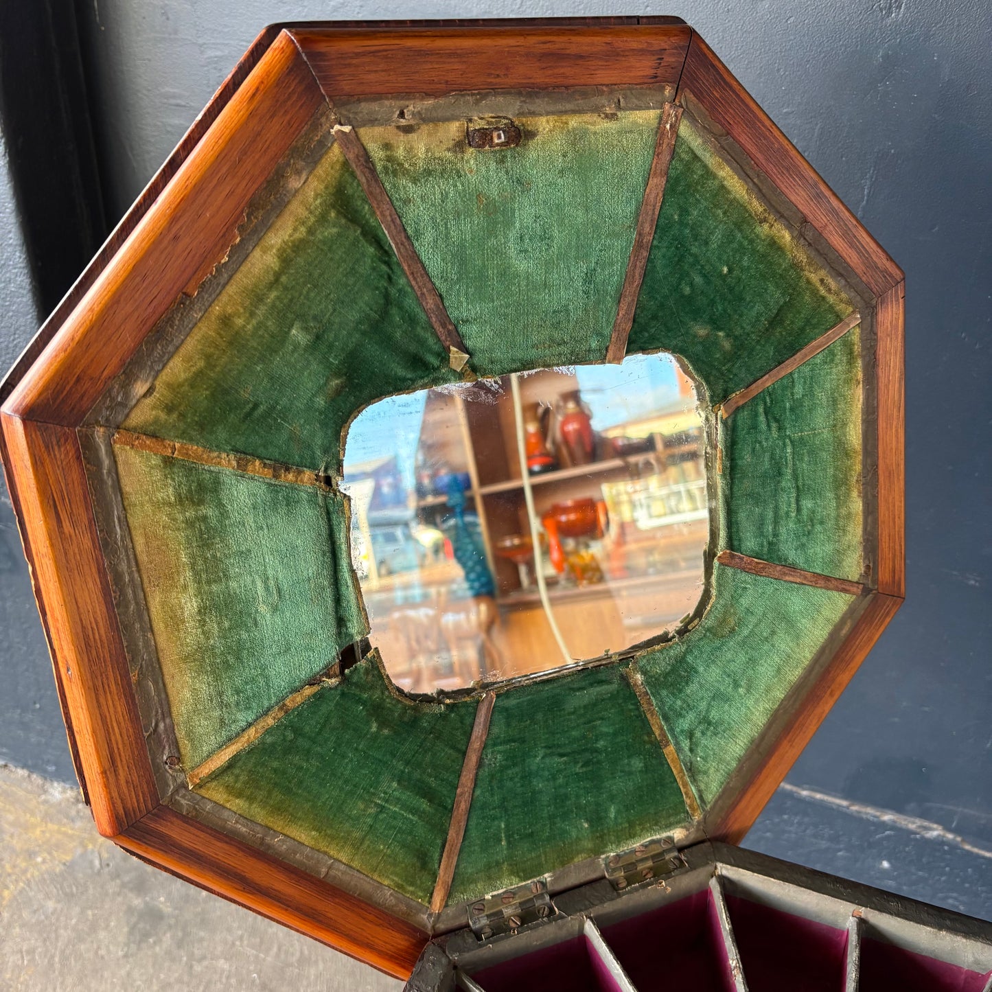 Hexagonal mirror with wooden frame and green velvet back on a dark background