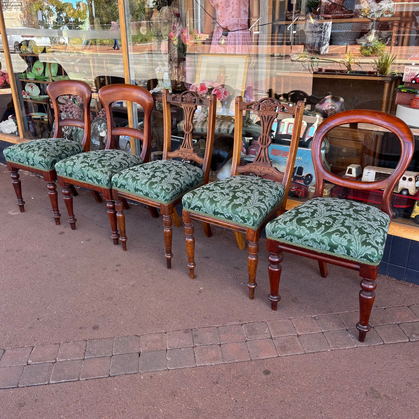 Set of wooden chairs with green patterned cushions on a pavement.