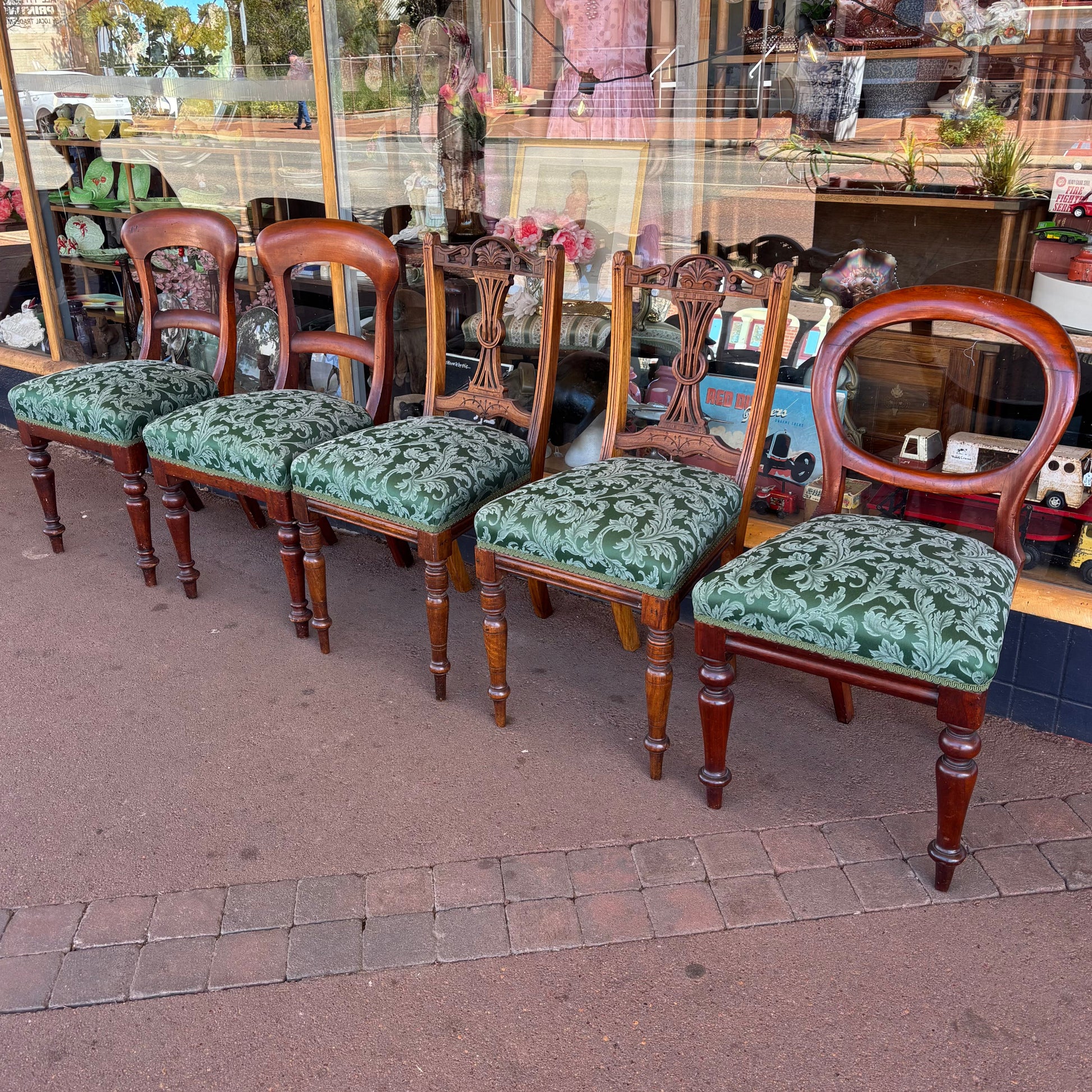 Set of wooden chairs with green patterned cushions on a pavement.