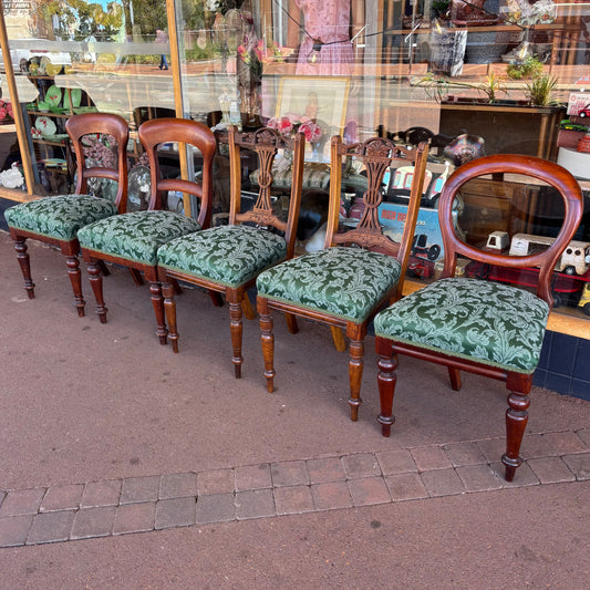 Set of wooden chairs with green patterned cushions on a pavement.
