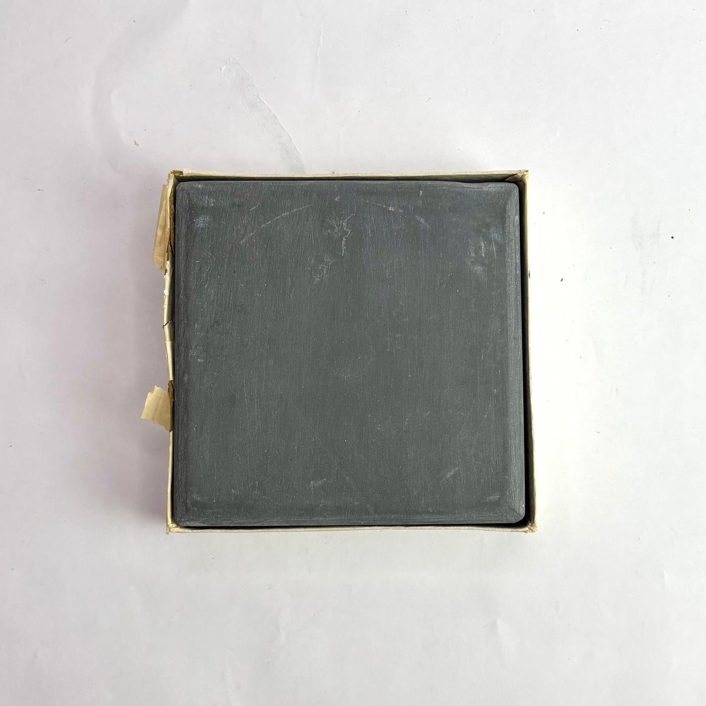 Square metal object with brass-colored border on a white background