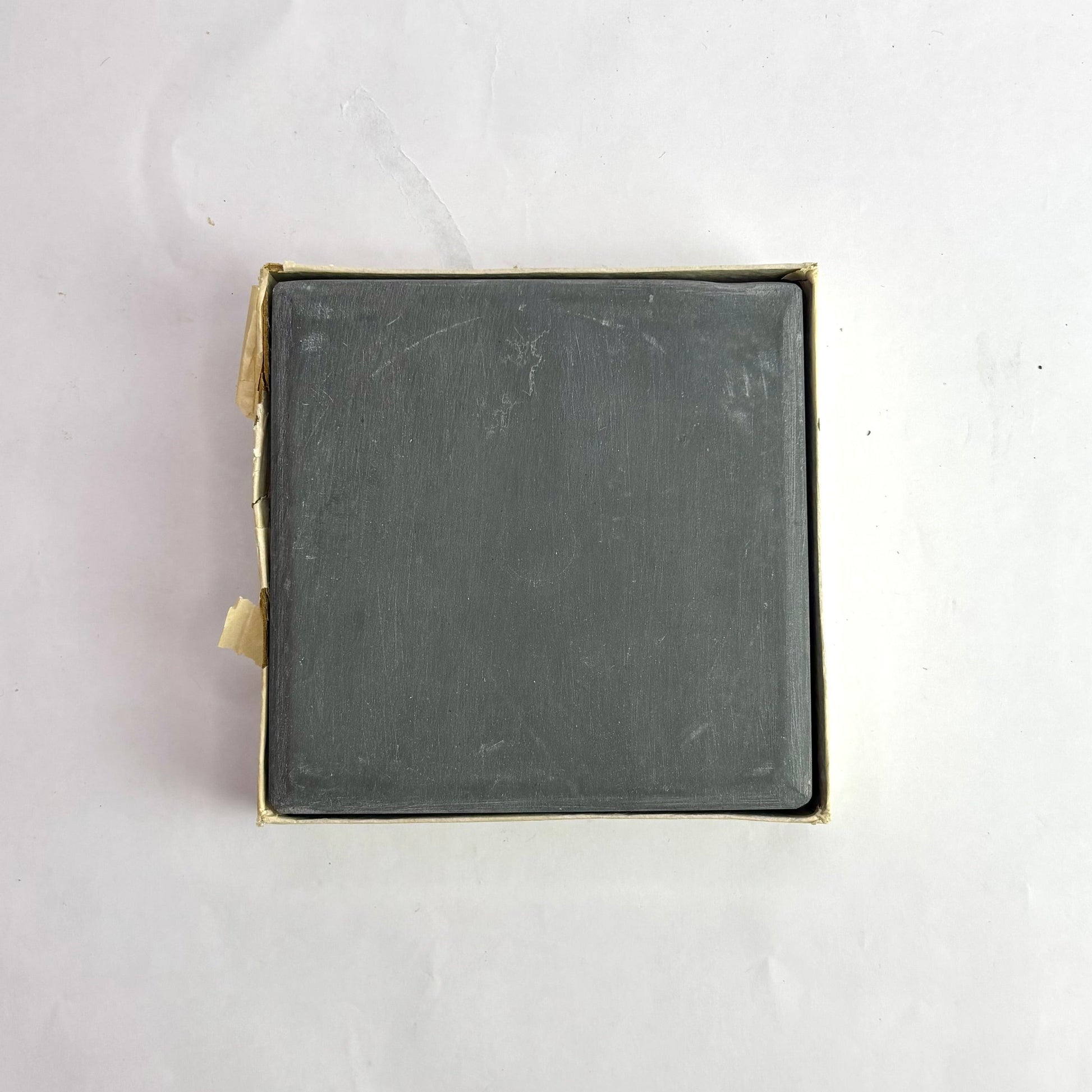 Square metal object with brass-colored border on a white background