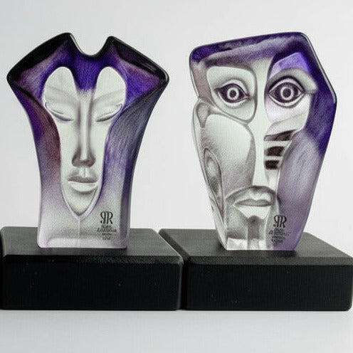 two abstract glass face sculptures on a black base against a white background