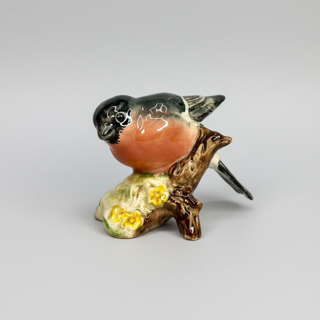 Small ceramic bird figurine on a branch with flowers against a gray background