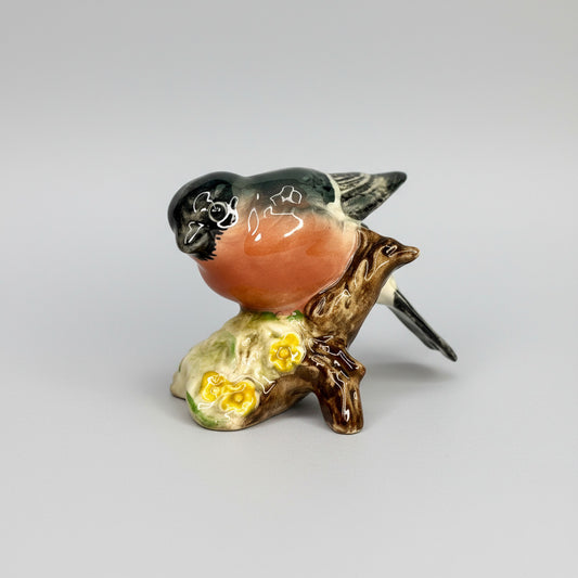 Small ceramic bird figurine on a branch with flowers against a gray background