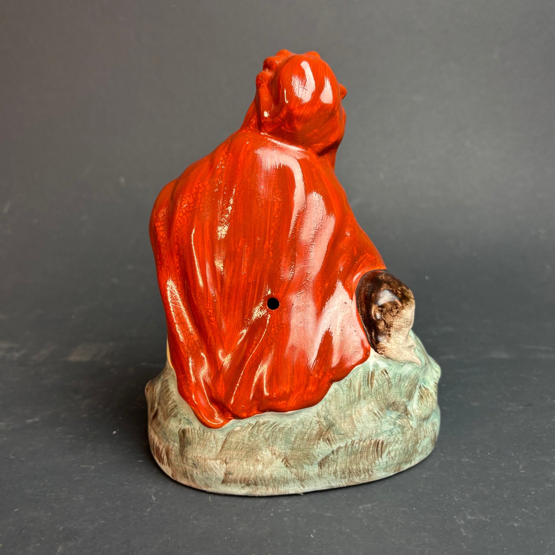 Ceramic figure of a person in red garment with a child on a gray background