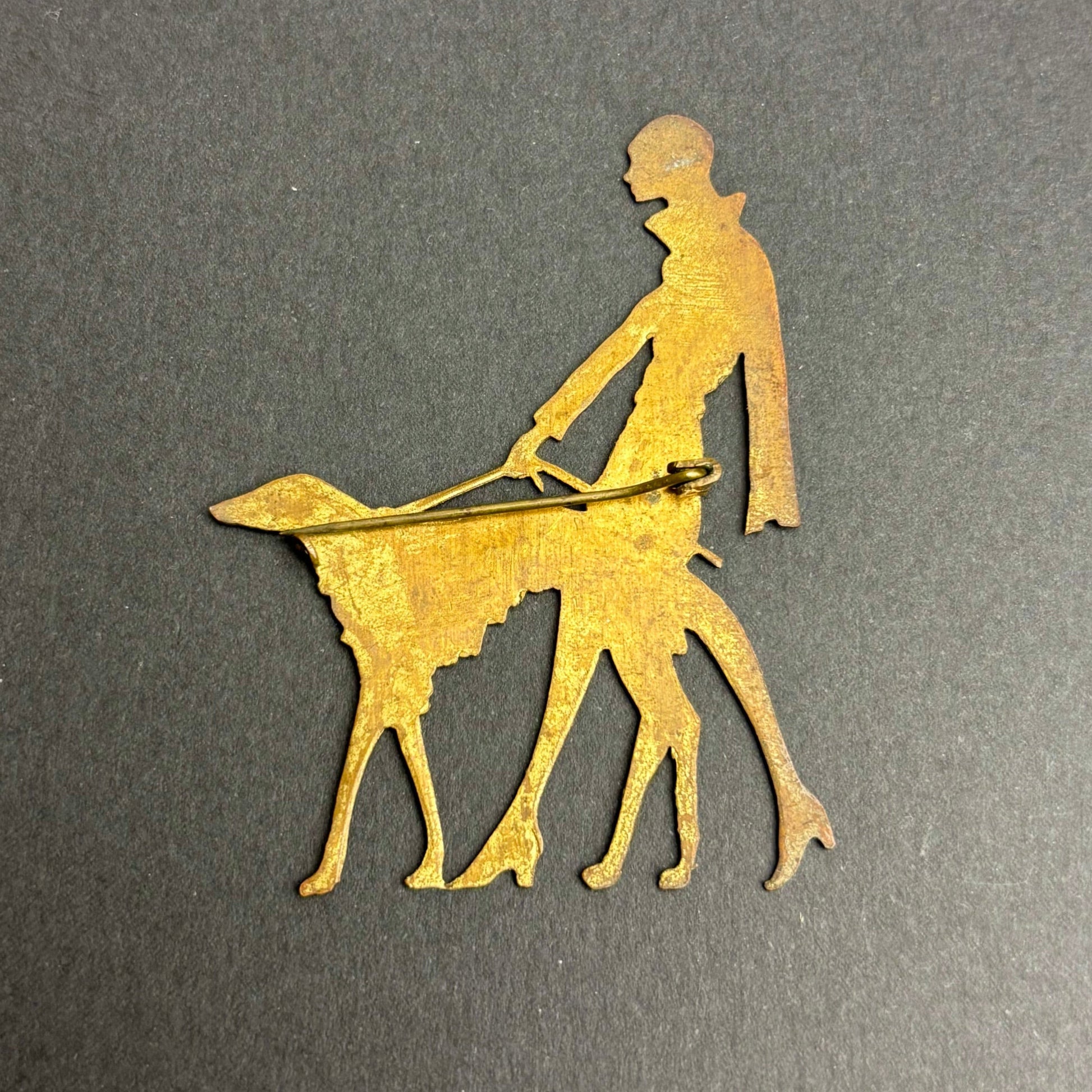 Gold metal cutout of a person walking a dog on a gray background