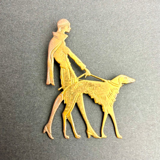 Gold-colored metal sculpture of a person walking a dog on a gray background