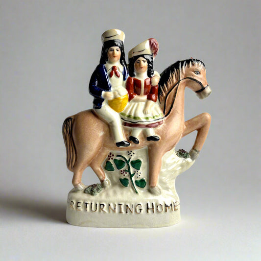 Decorative figurine of two people on a horse with 'Returning Home' text on a plain background