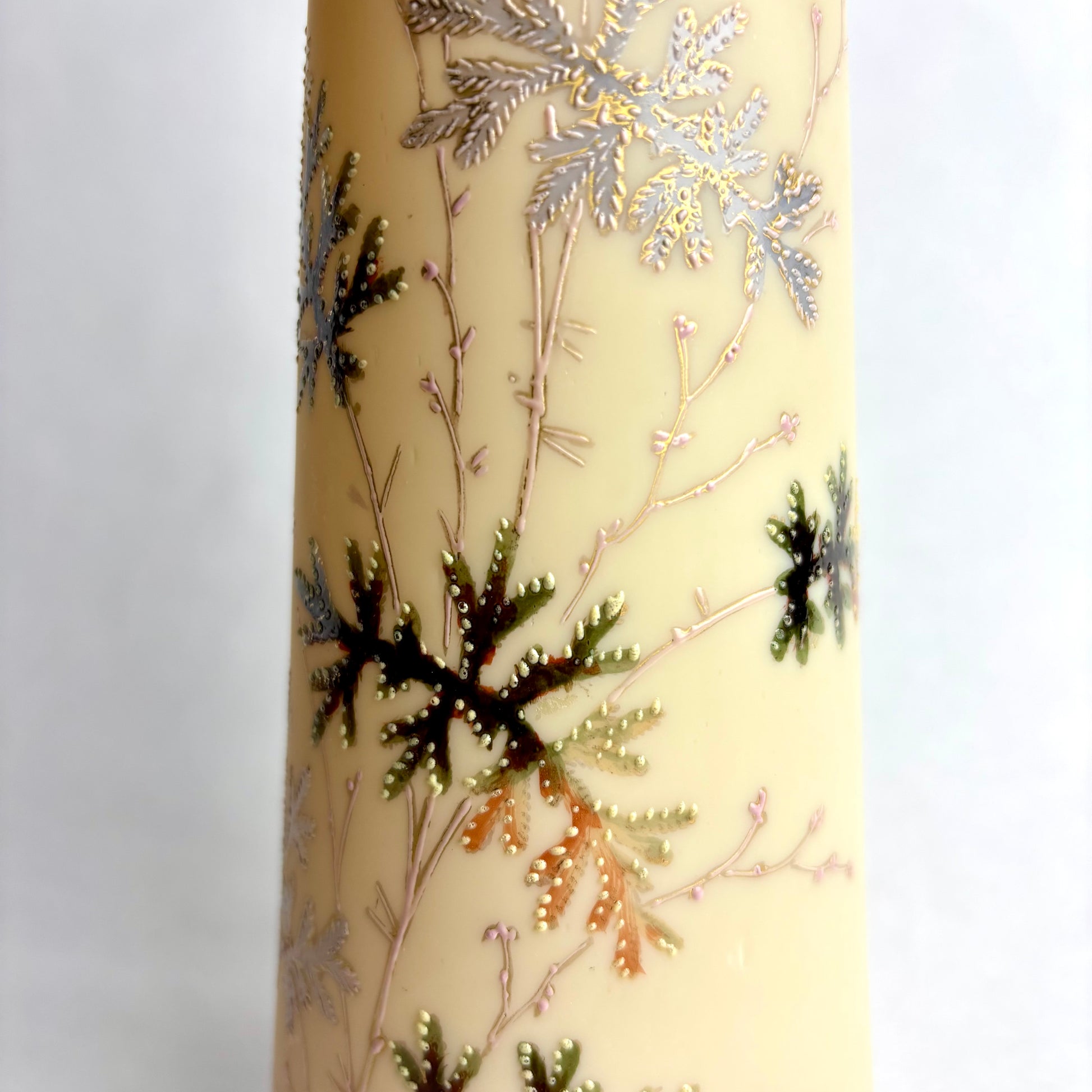 Decorative candle with metallic leaf patterns on a beige background