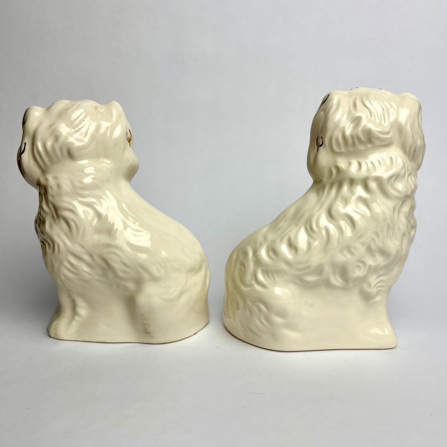 Two cream-colored ceramic dog figurines on a light gray background