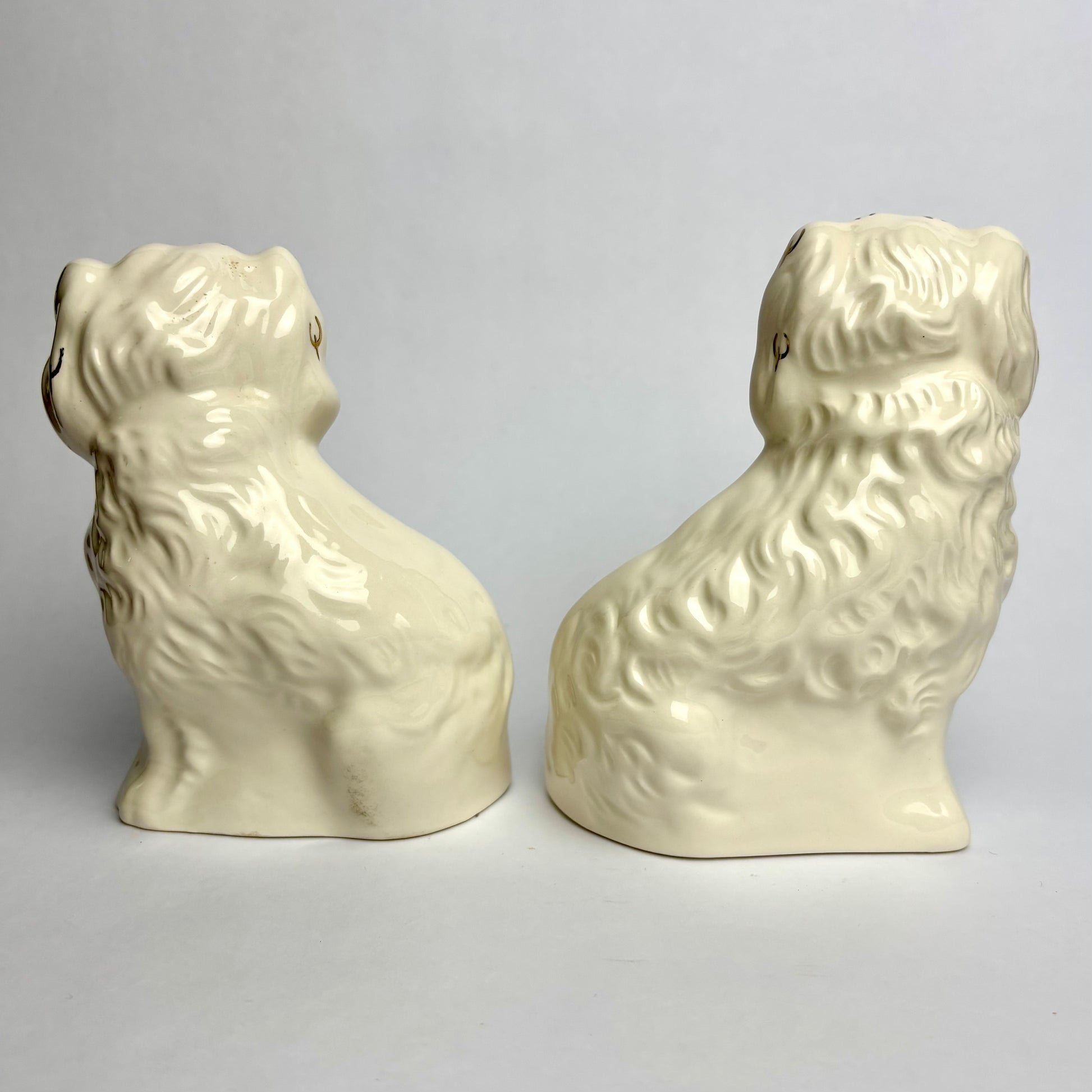 Two cream-colored ceramic dog figurines on a light gray background